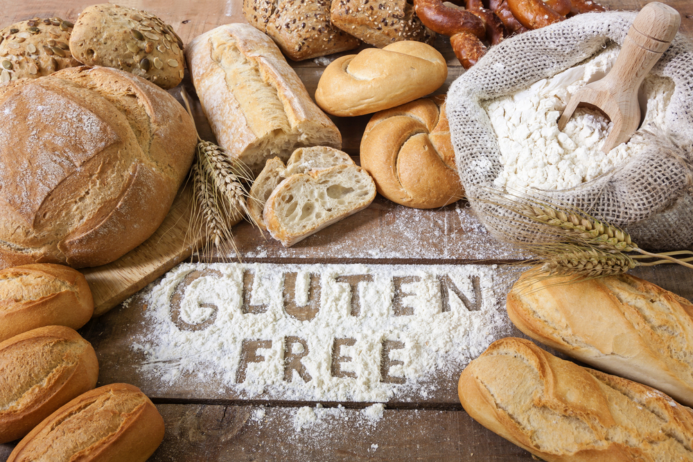 Gluten free written in flour on a table surround with gluten free loaves of bread